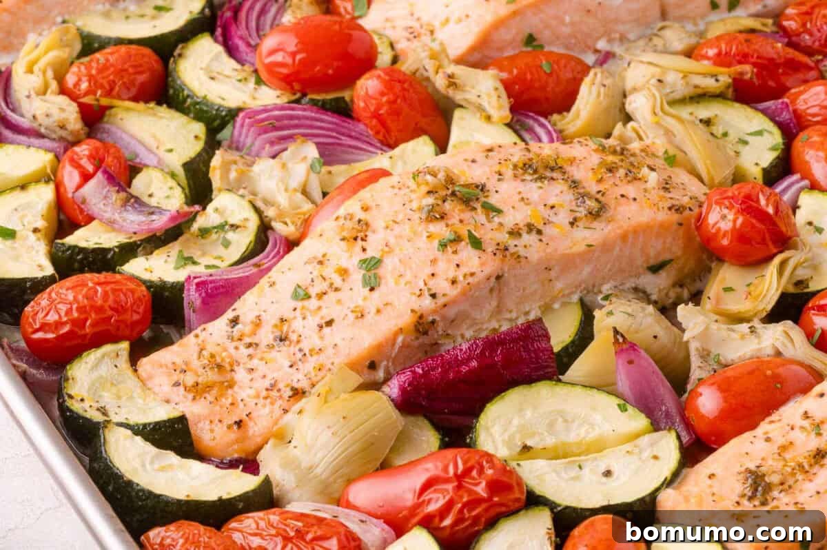 Baked salmon with roasted cherry tomatoes, zucchini, red onion, and artichoke hearts, seasoned with herbs.