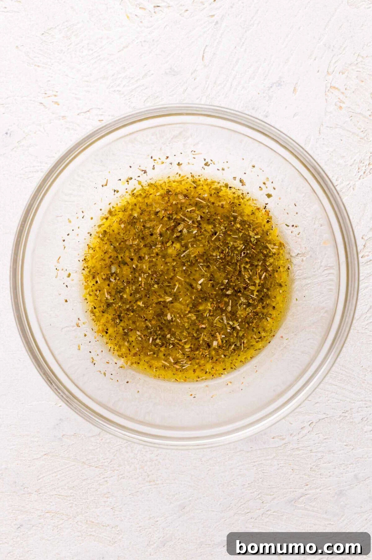 Mixture of olive oil and dried herbs in a glass bowl.