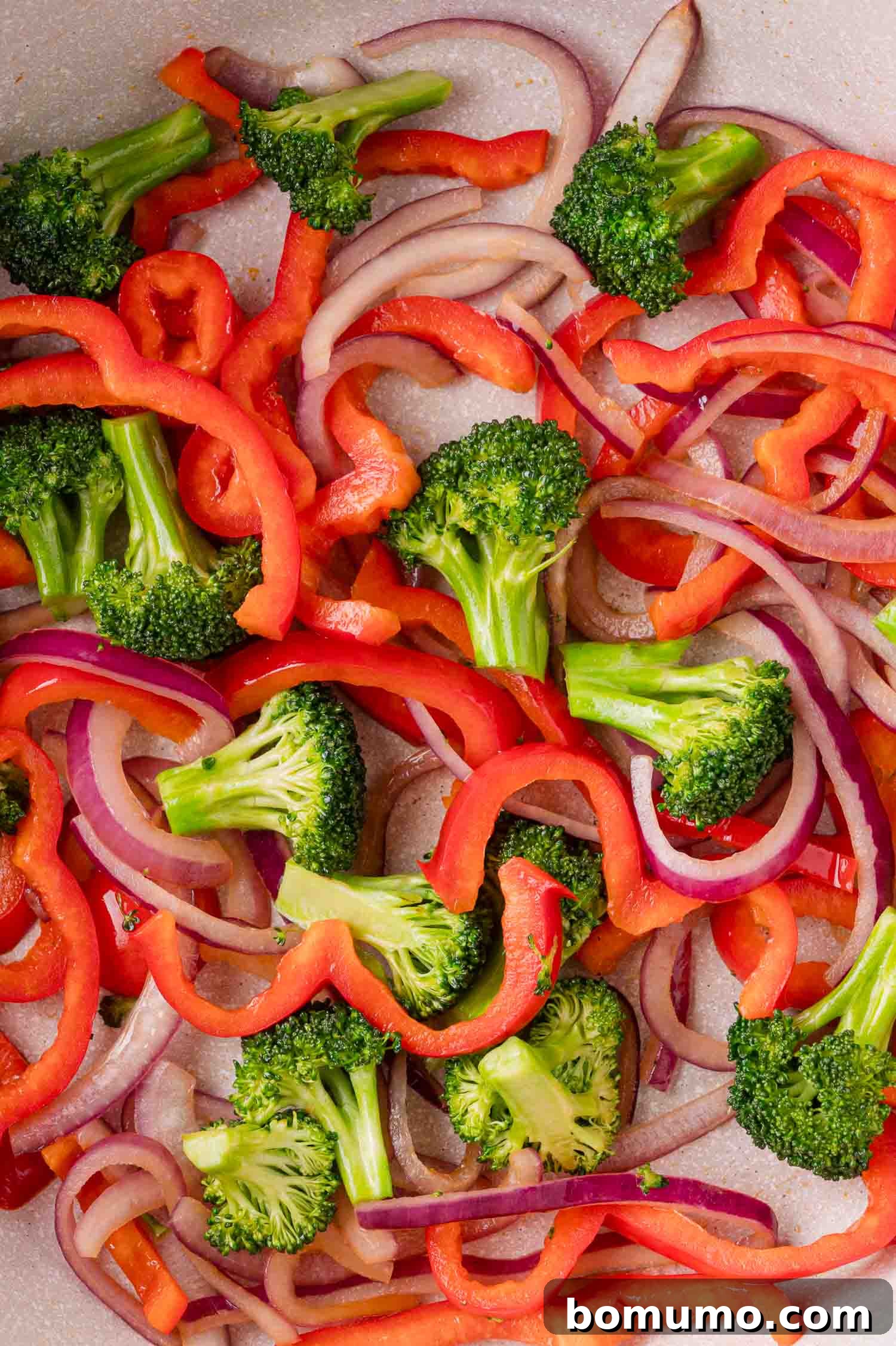 Stir-Frying Veggies: Sliced red bell peppers, broccoli, and red onion in a pan.
