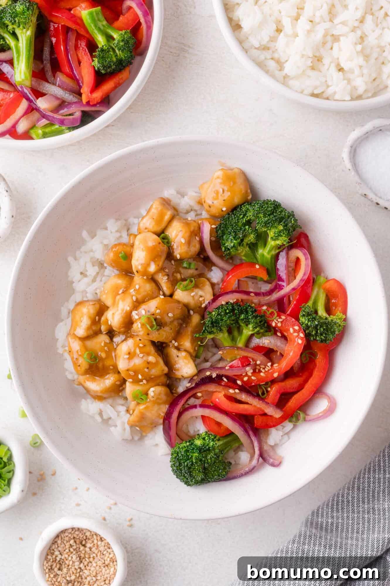 Assembled Teriyaki Chicken Bowl: White rice topped with teriyaki chicken, broccoli, bell peppers, and red onions.
