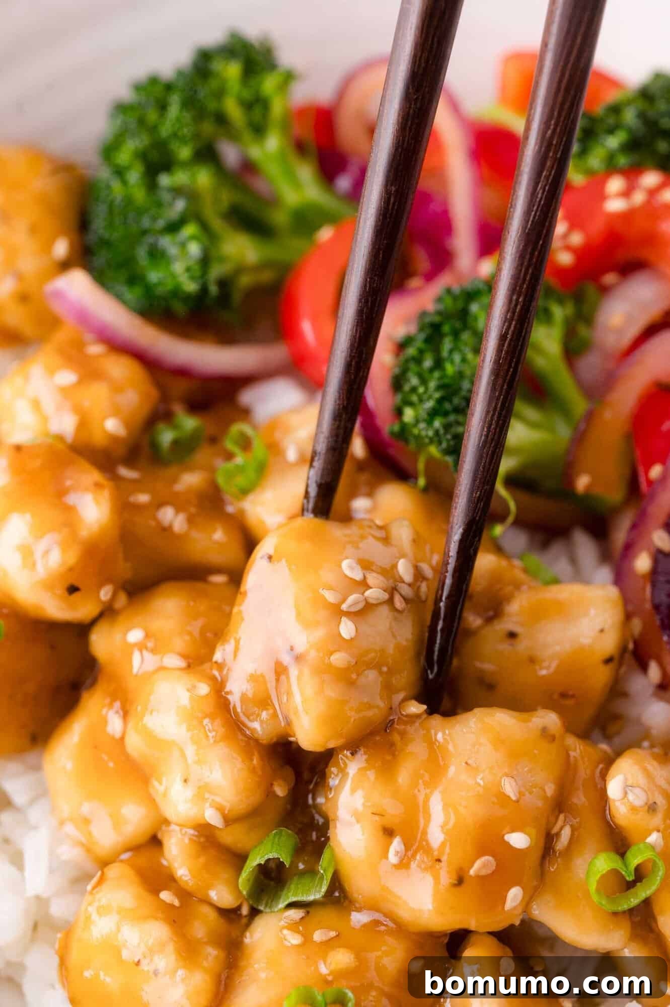 Close-Up Shot: Chopsticks holding a piece of teriyaki chicken over white rice.