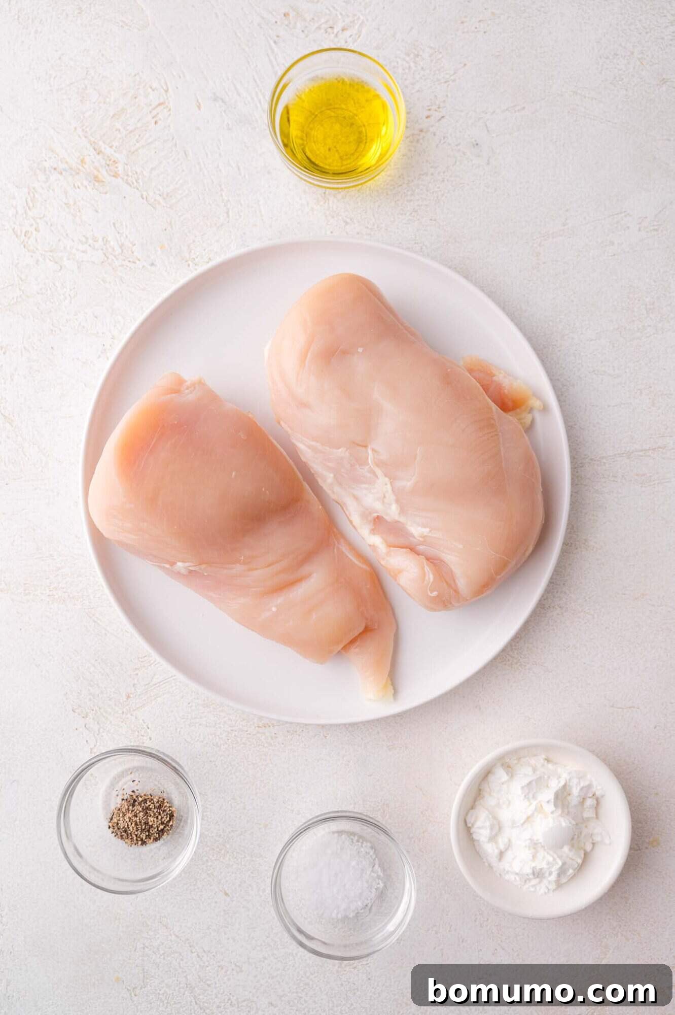 Raw Chicken Prep: Raw chicken breasts on a plate, surrounded by bowls of olive oil, pepper, salt, and cornstarch.