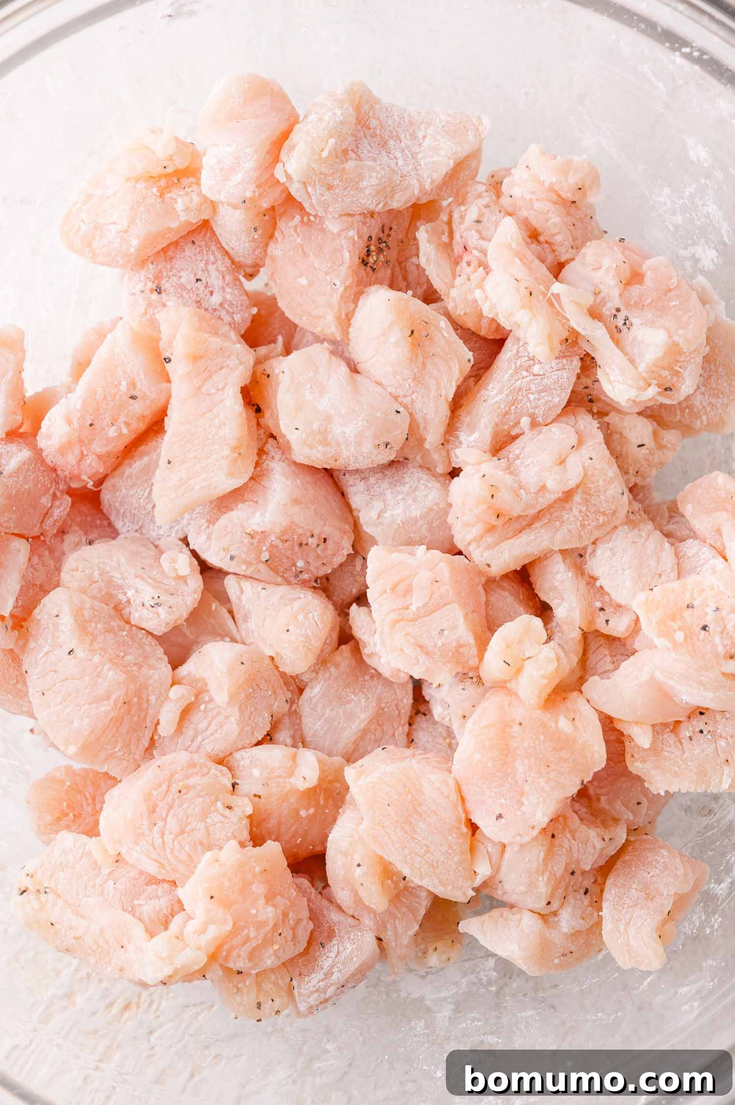 Cornstarch Coated Chicken: Cubed chicken pieces in a bowl, lightly coated with cornstarch, salt, and pepper.