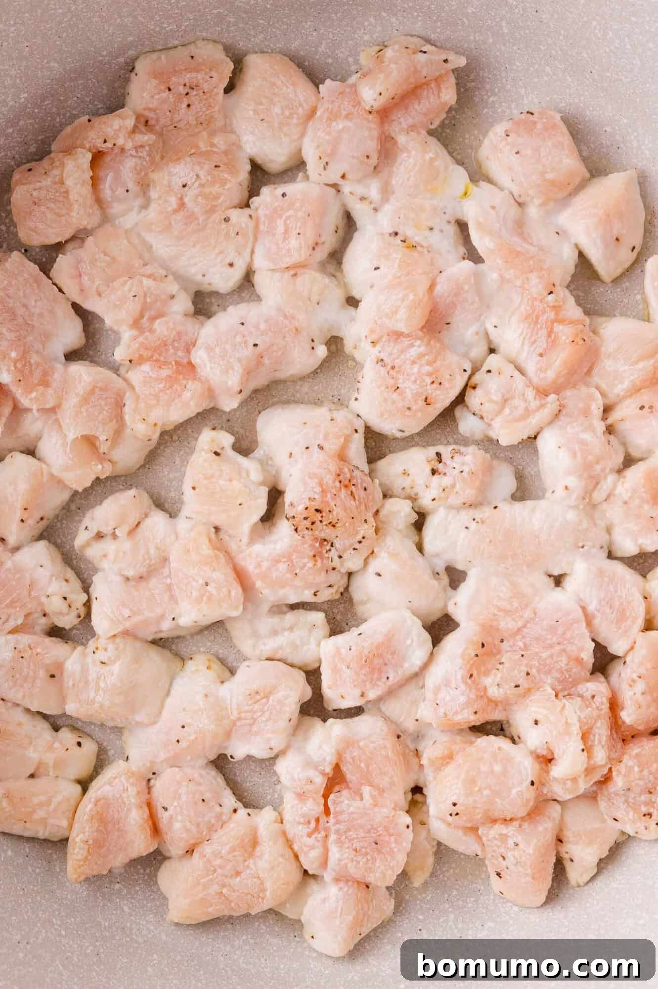 Cooking Chicken: Cubed chicken pieces being cooked in a pan with browned edges.