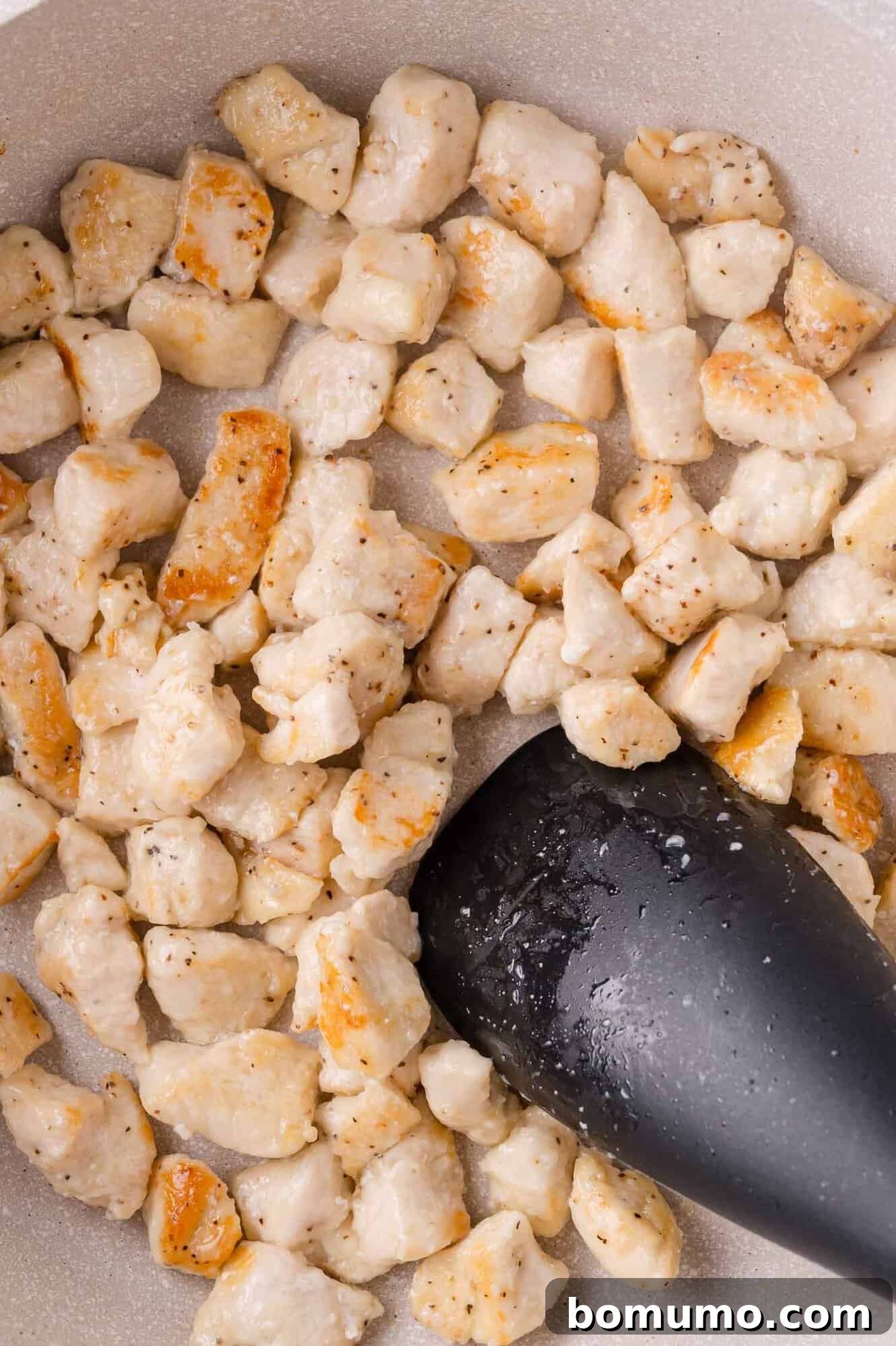Stirring Chicken: Cooked diced chicken pieces being stirred in a pan with a spatula.