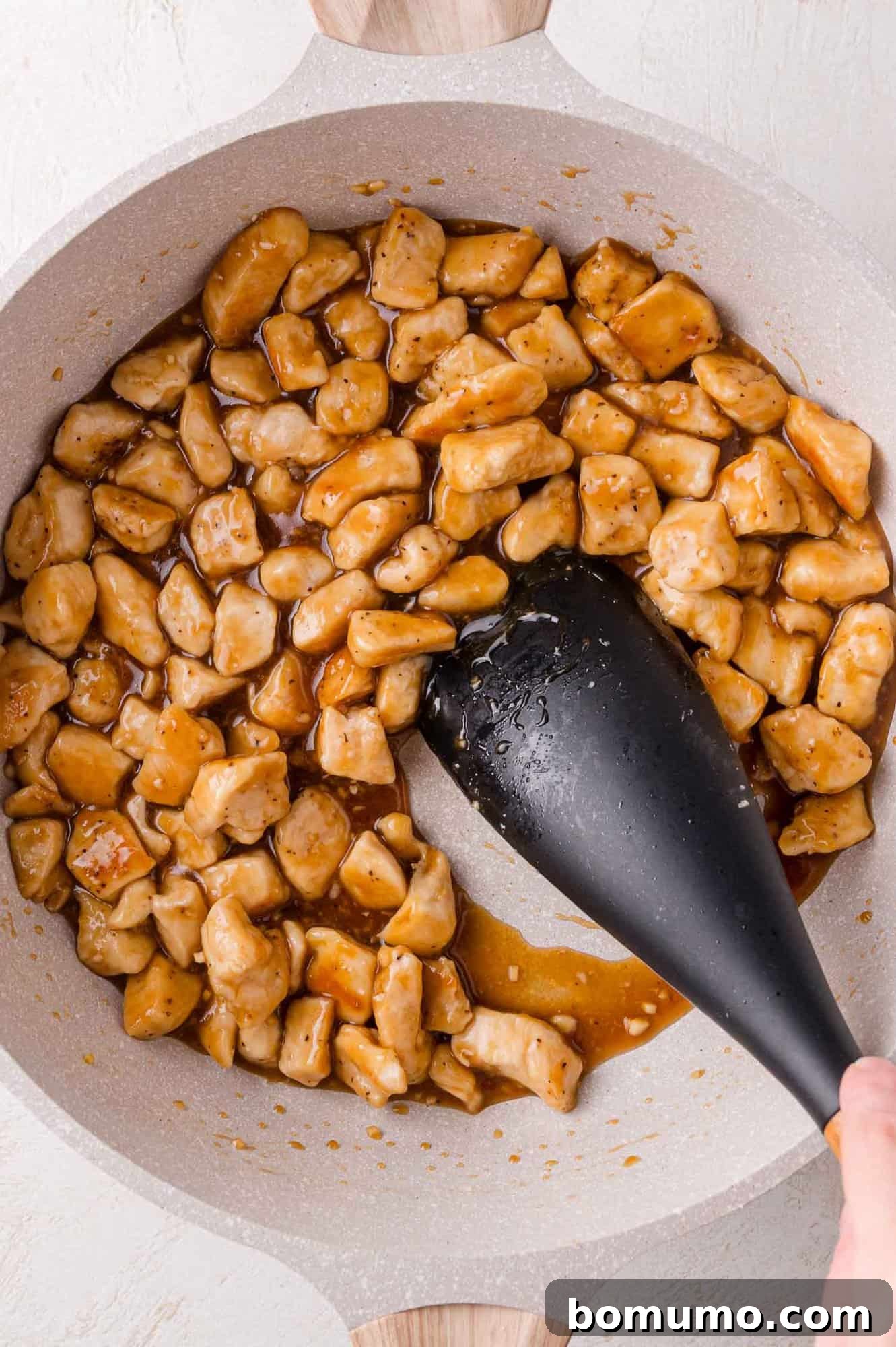 Sauce Thickening: Chunks of chicken coated in teriyaki sauce being stirred with a spatula in a pan.