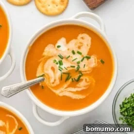 Carrot soup in a white bowl topped with chives and a swirl of cream.