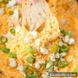 Warm and cheesy Crockpot Buffalo Chicken Dip with a crusty piece of bread being dipped in.