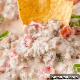 Close-up of sausage dip being scooped up with a crunchy tortilla chip.