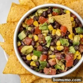 Overhead view of fresh black bean, creamy avocado, and sweet corn salad served with crispy tortilla chips.