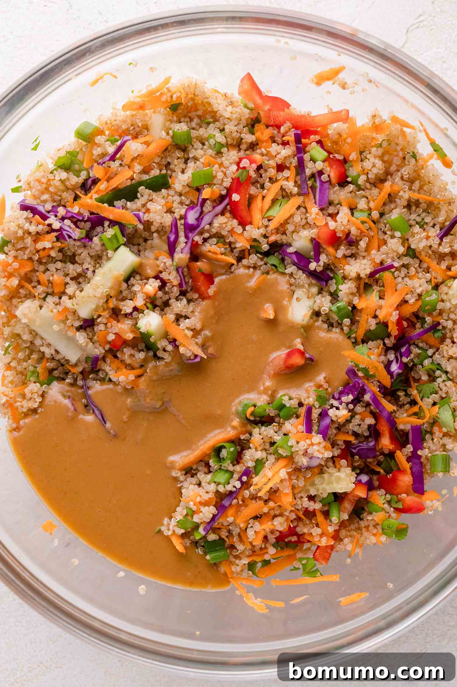Adding peanut dressing to the quinoa and vegetable mixture
