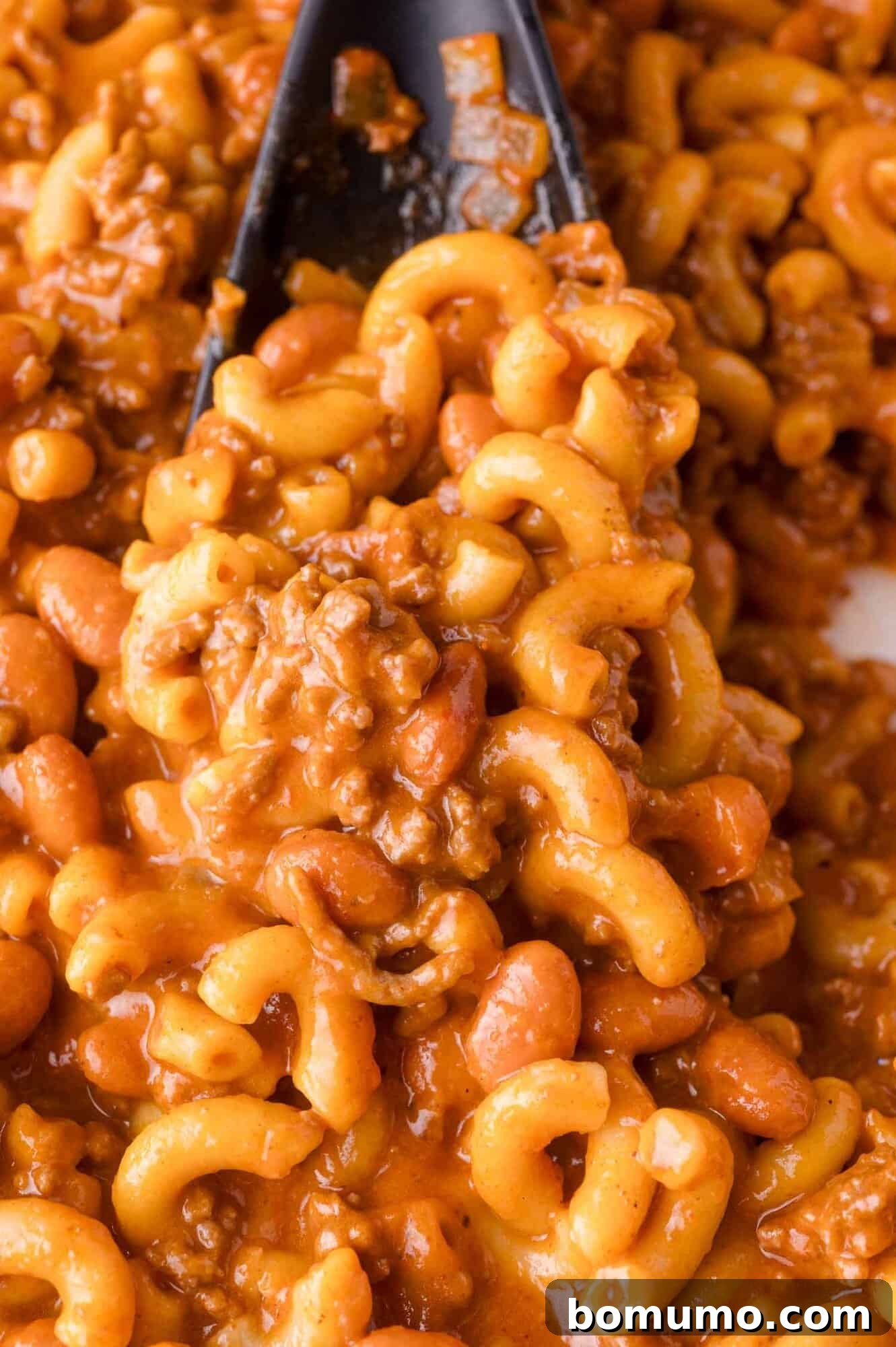 Chili mac close-up featuring pasta, ground beef, beans, and tomato-based sauce served with a spoon.