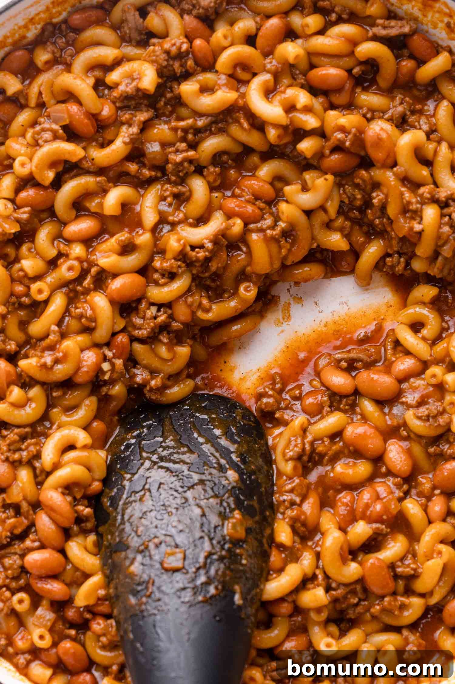 Stirring macaroni, beef, and beans in a pot.