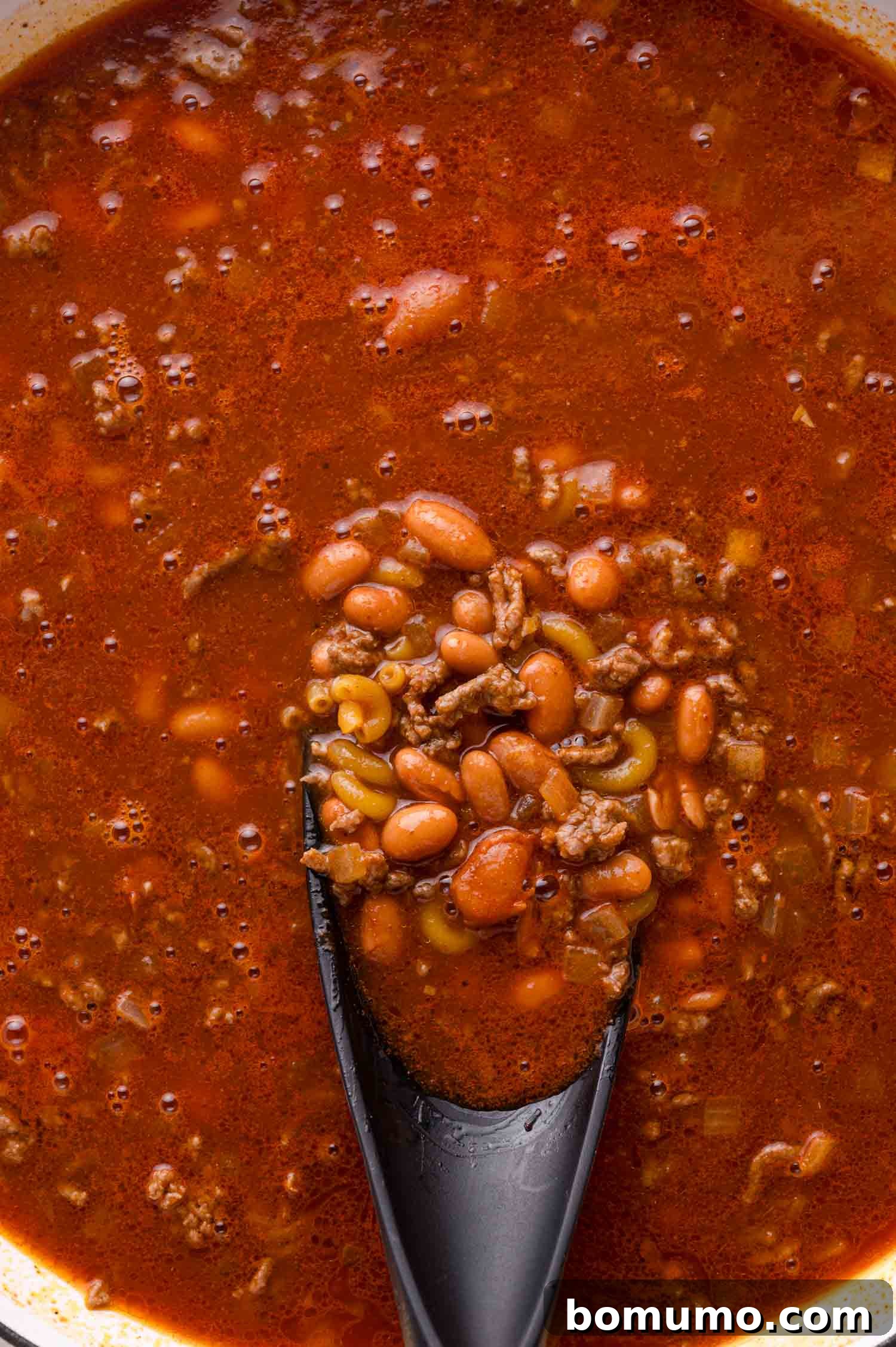 Spoon scooping chili with ground beef and beans.