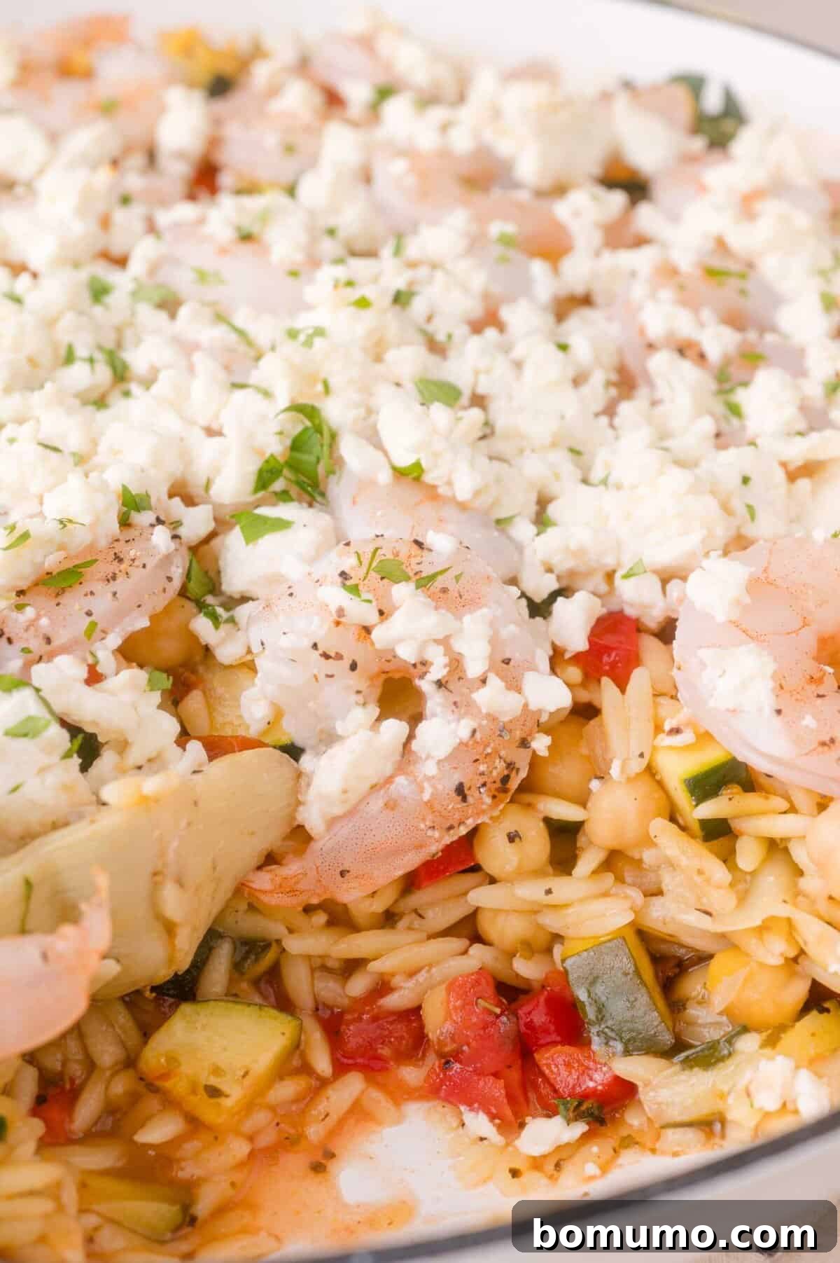 Close-up of baked shrimp and vegetable orzo with feta and herbs
