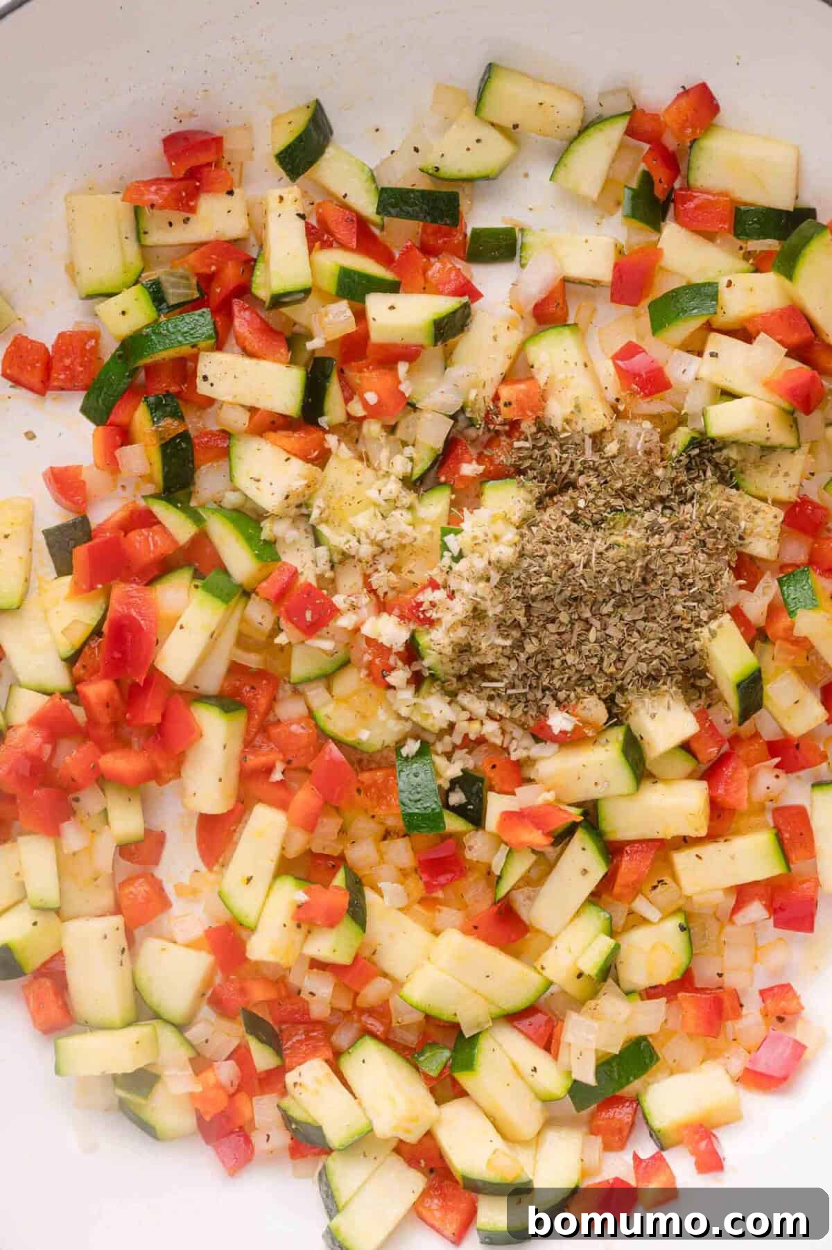 Adding garlic and oregano to sautéed vegetables