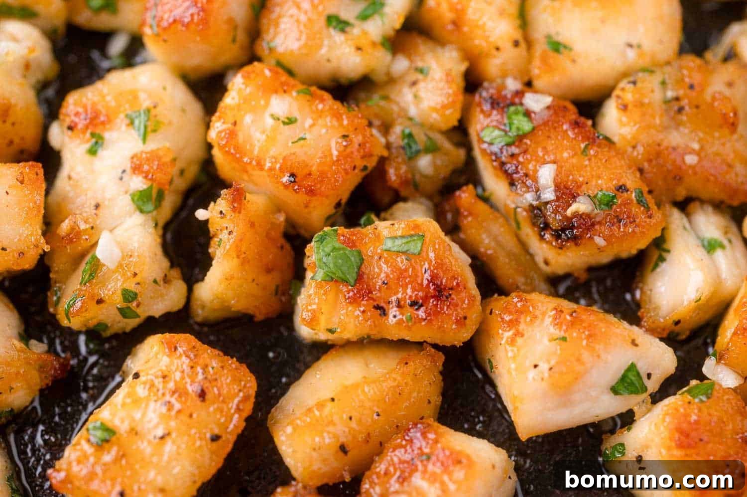 Close-up of golden-brown, seasoned chicken pieces cooking in a pan.