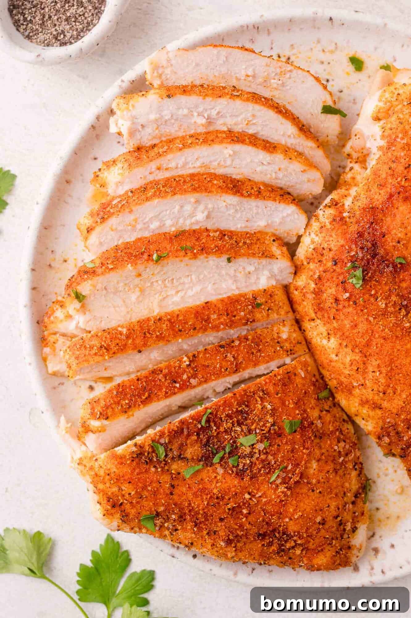 Perfectly sliced and seasoned baked chicken breast on a plate, garnished with fresh herbs.