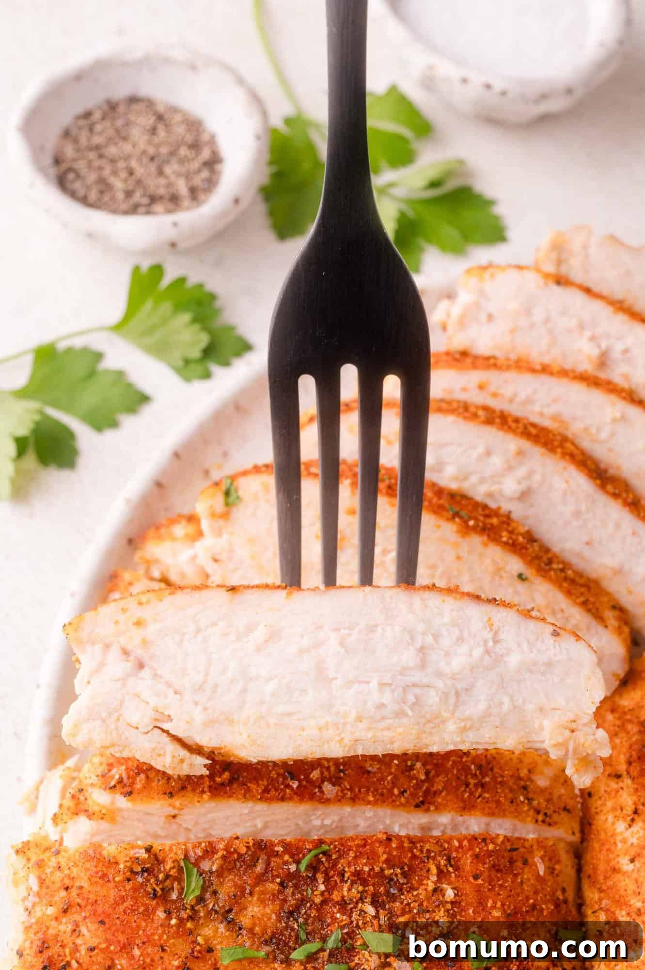 Close-up of seasoned baked chicken breast on a fork.