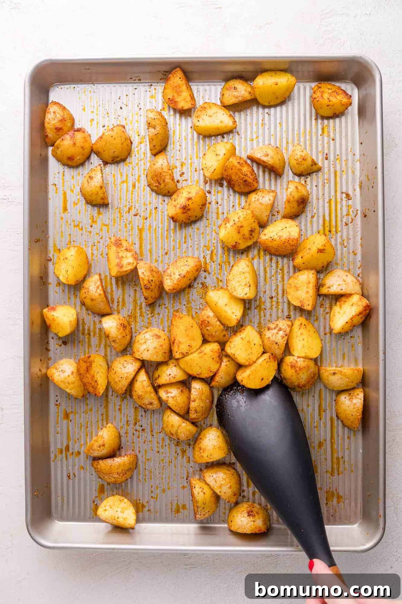 Seasoned potatoes being stirred on a baking sheet.