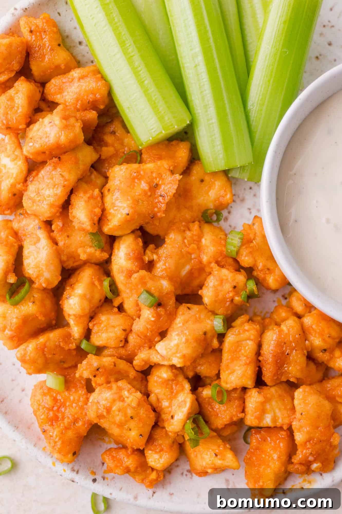 Buffalo Chicken Poppers 2 Plate of buffalo chicken bites with green onions, celery sticks, and a bowl of ranch dipping sauce.