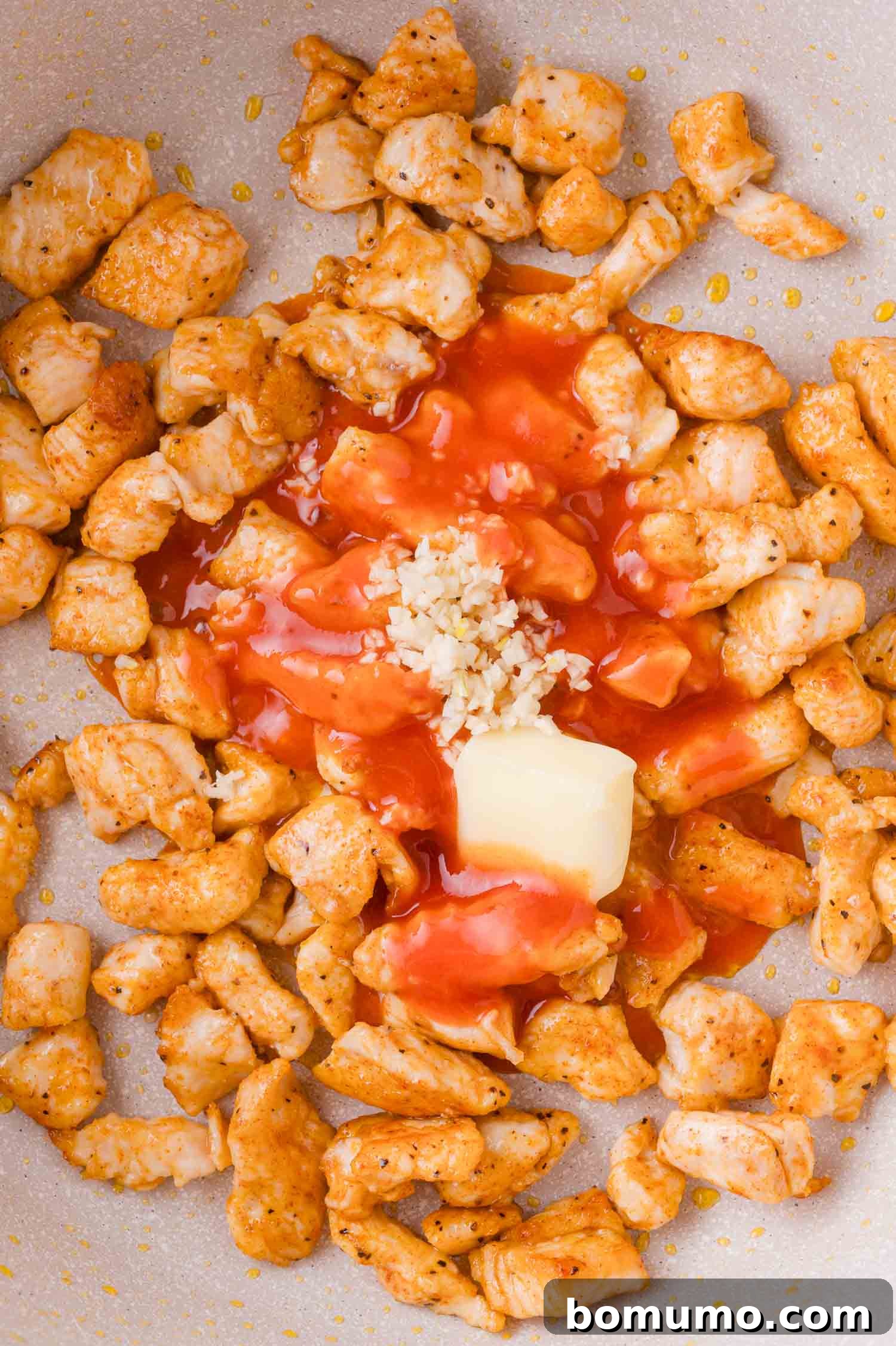 Buffalo Chicken Poppers 11 Seasoned, cooked chicken pieces in a pan with hot sauce, minced garlic, and a pat of butter.