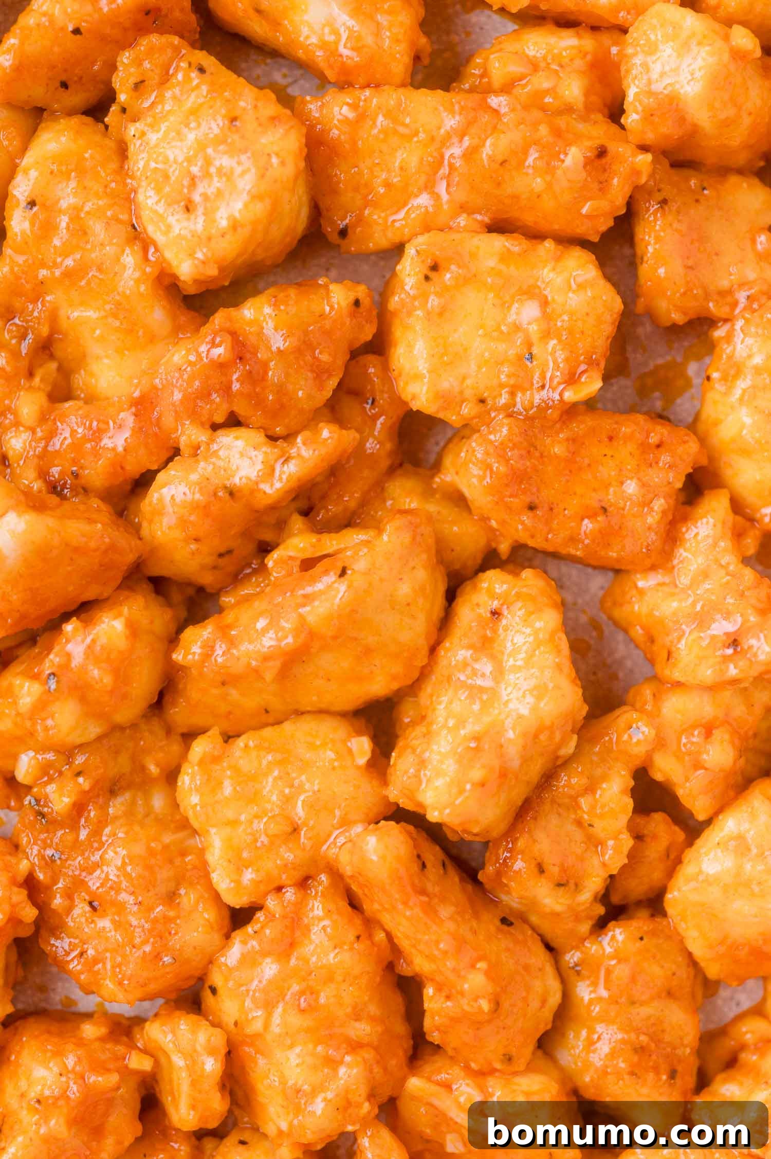 Buffalo Chicken Poppers 12 Close-up view of golden, sauced chicken pieces on a sheet, showing texture and seasoning.