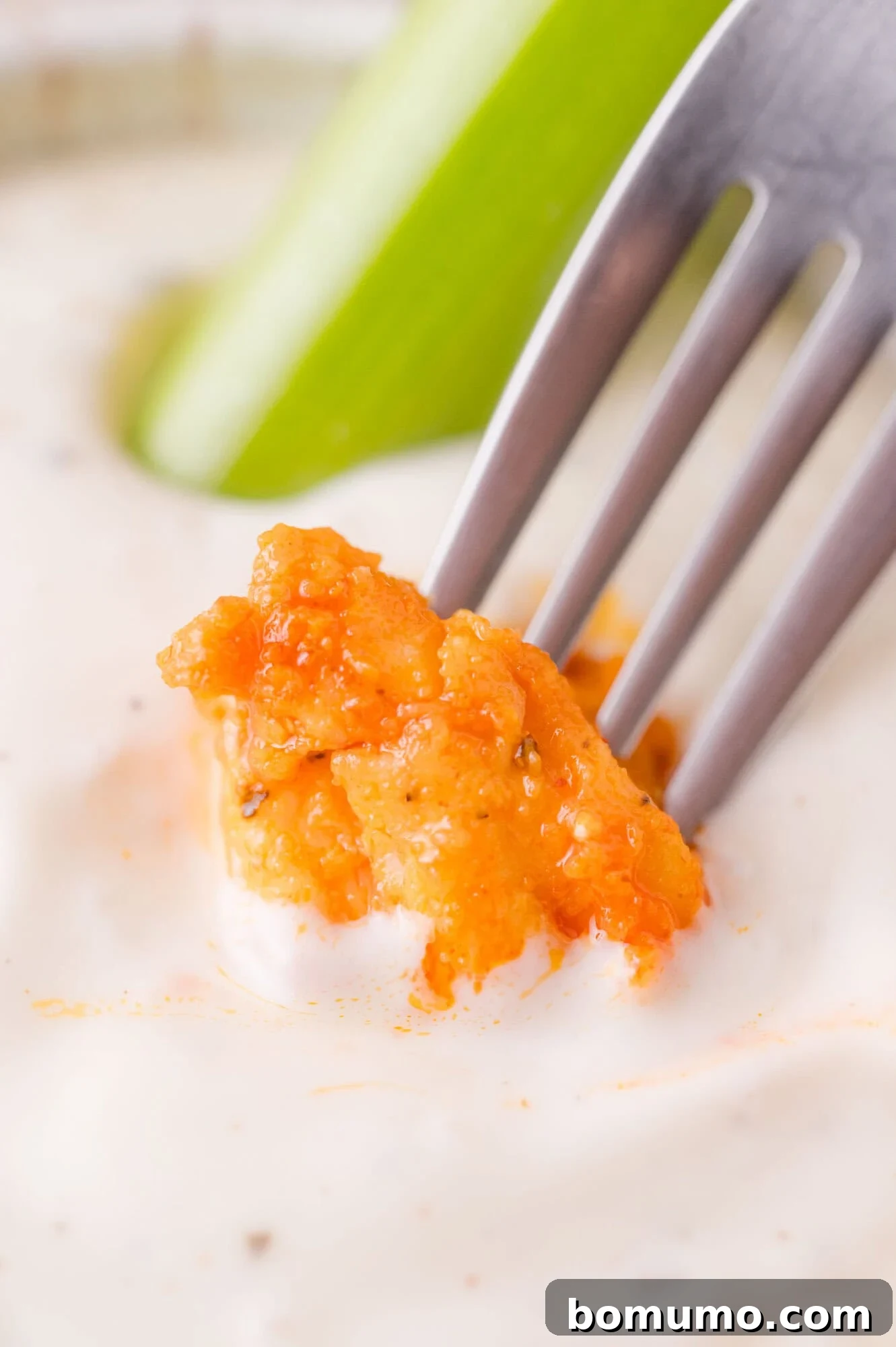 Buffalo Chicken Poppers 14 A fork holds a piece of buffalo chicken dipped in creamy ranch dressing, with a celery stick in the background.