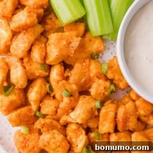 Plate of buffalo chicken bites garnished with chopped green onions, served with celery sticks and a cup of ranch dressing.