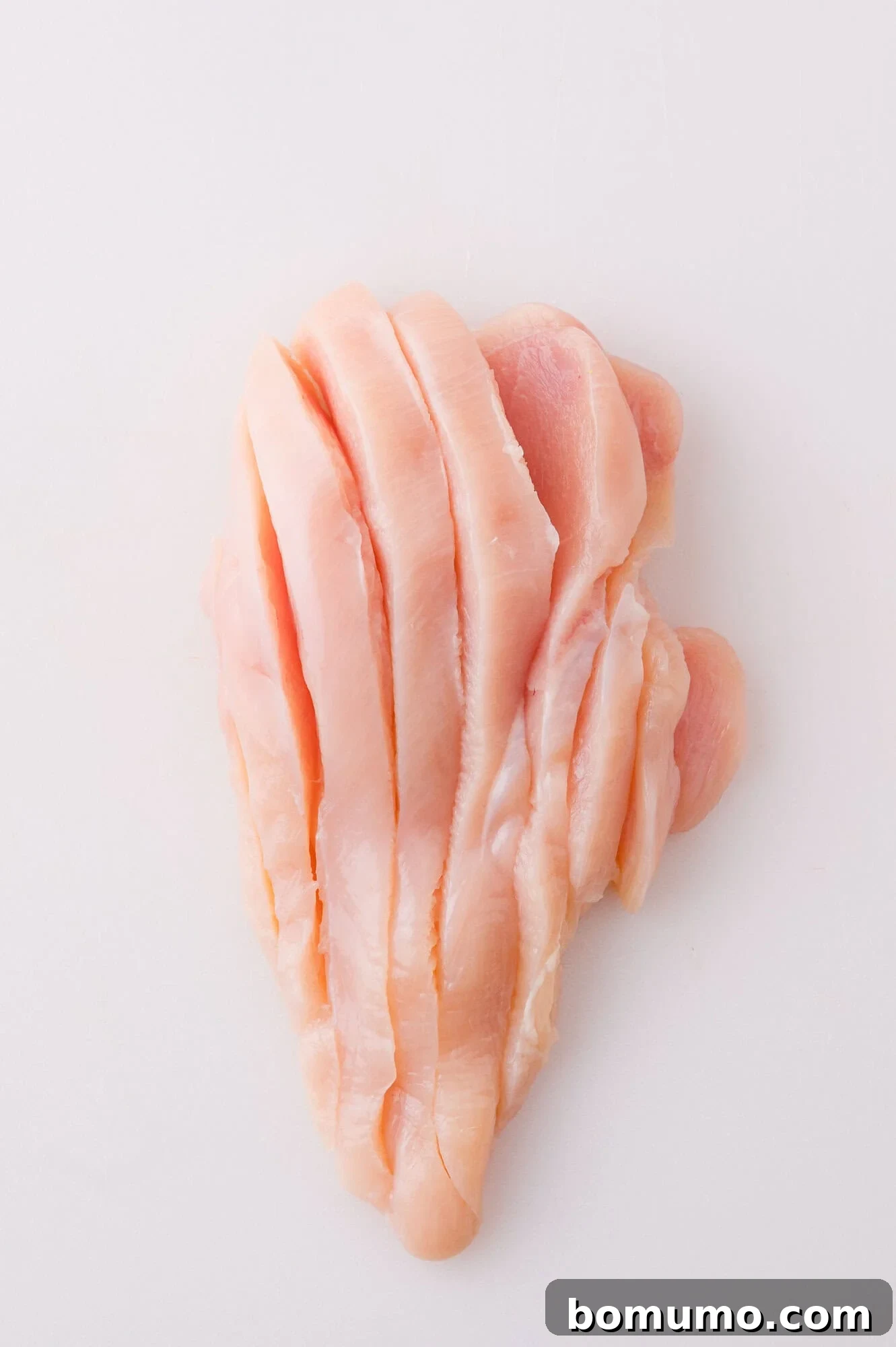 Buffalo Chicken Poppers 6 Raw, boneless chicken breast sliced into strips on a white surface.