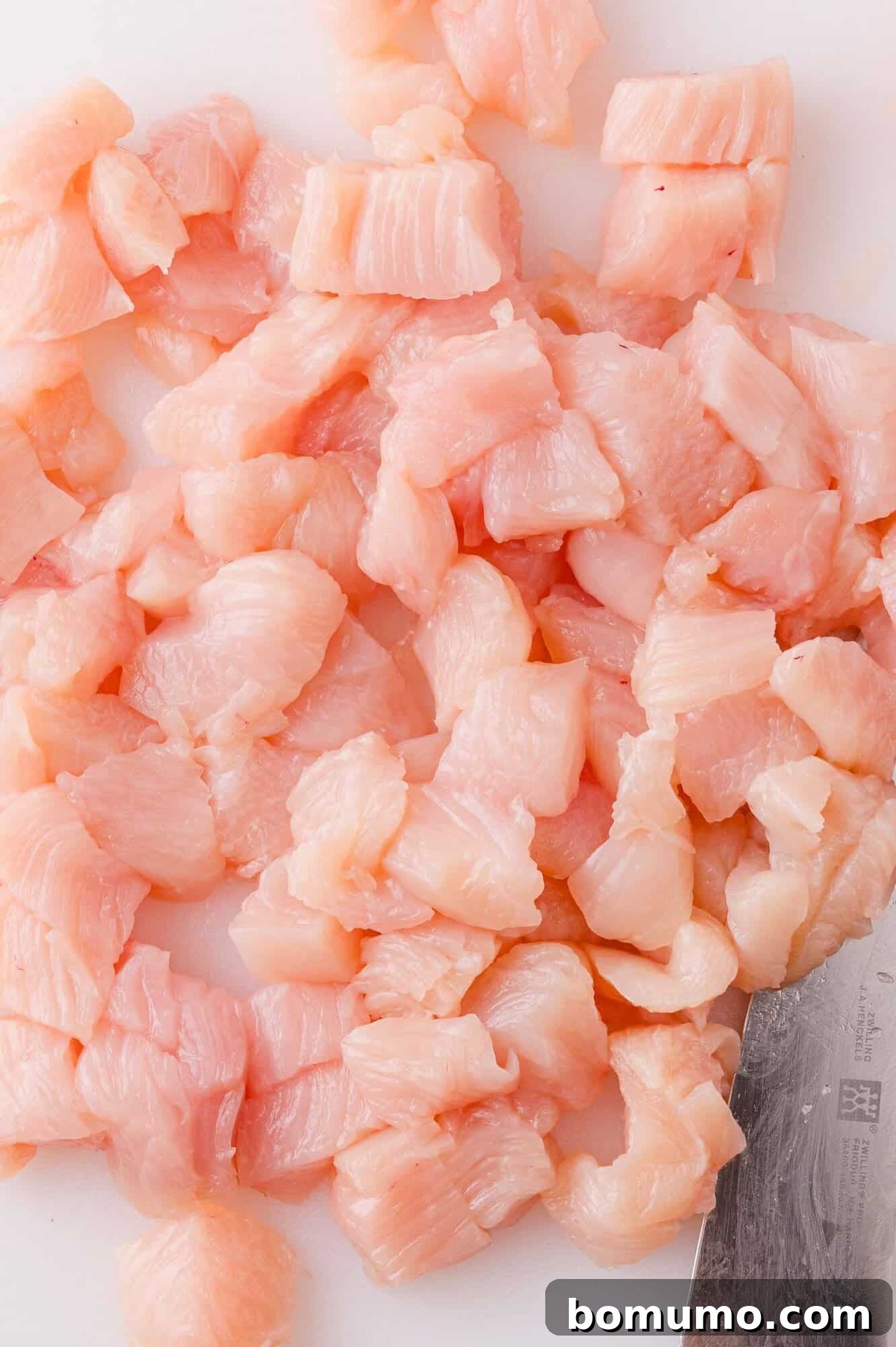Buffalo Chicken Poppers 7 Diced raw chicken breast pieces on a white cutting board with a metal knife visible in the corner.