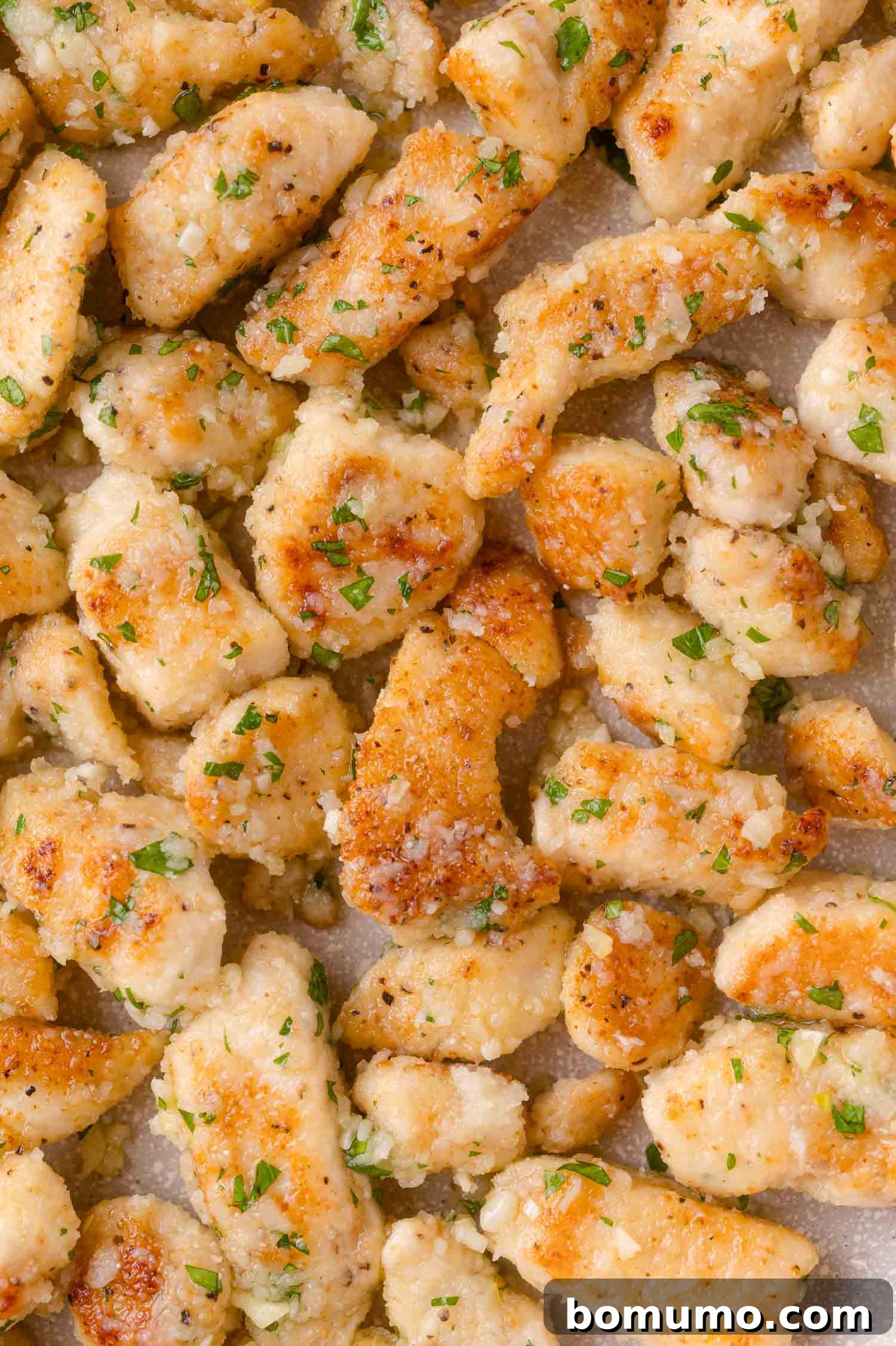 Close-up of cooked, golden-brown chicken pieces garnished with chopped herbs on a flat surface.