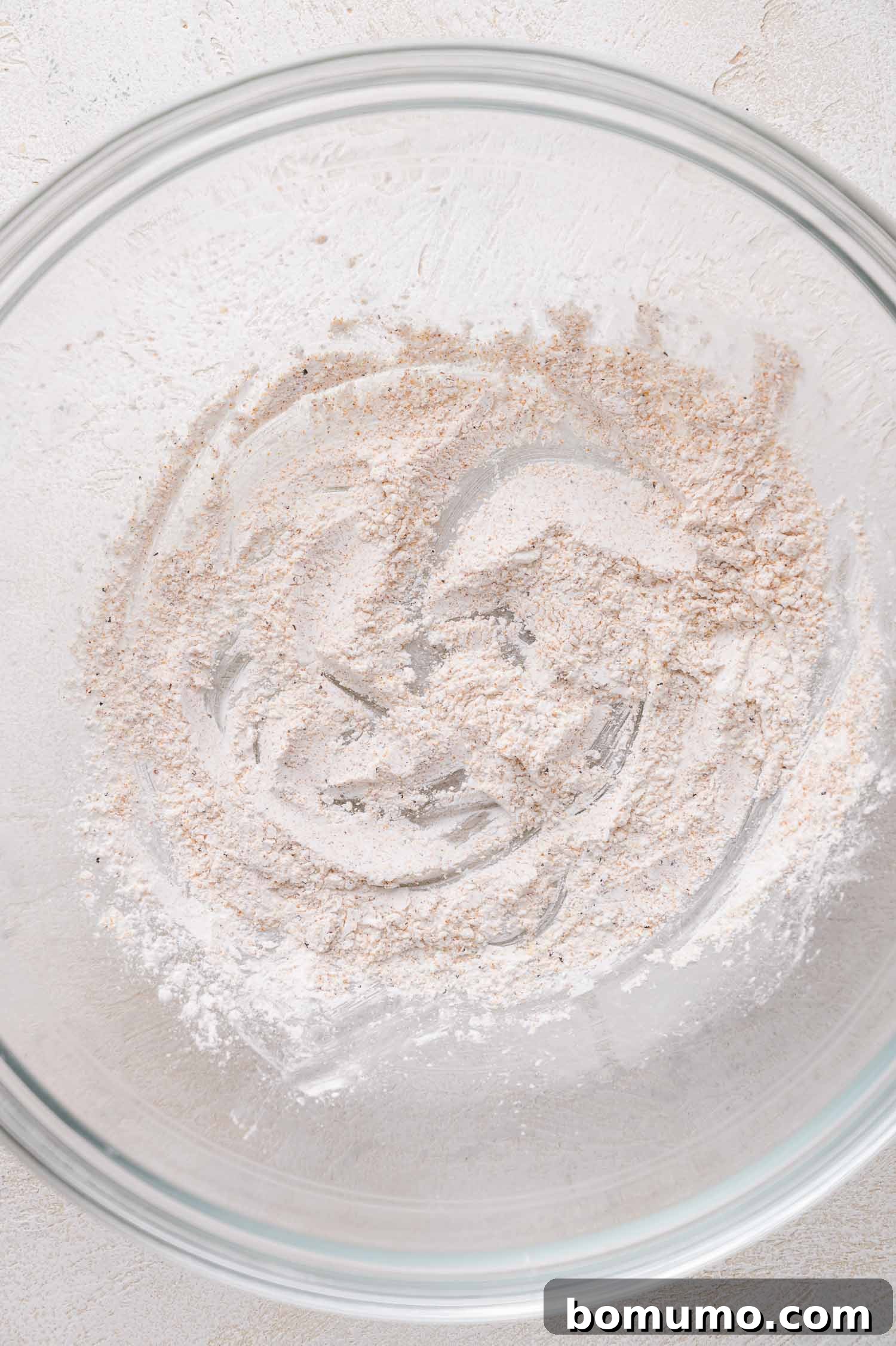 A clear glass mixing bowl contains a small amount of cornstarch on the bottom, lightly spread across the surface.