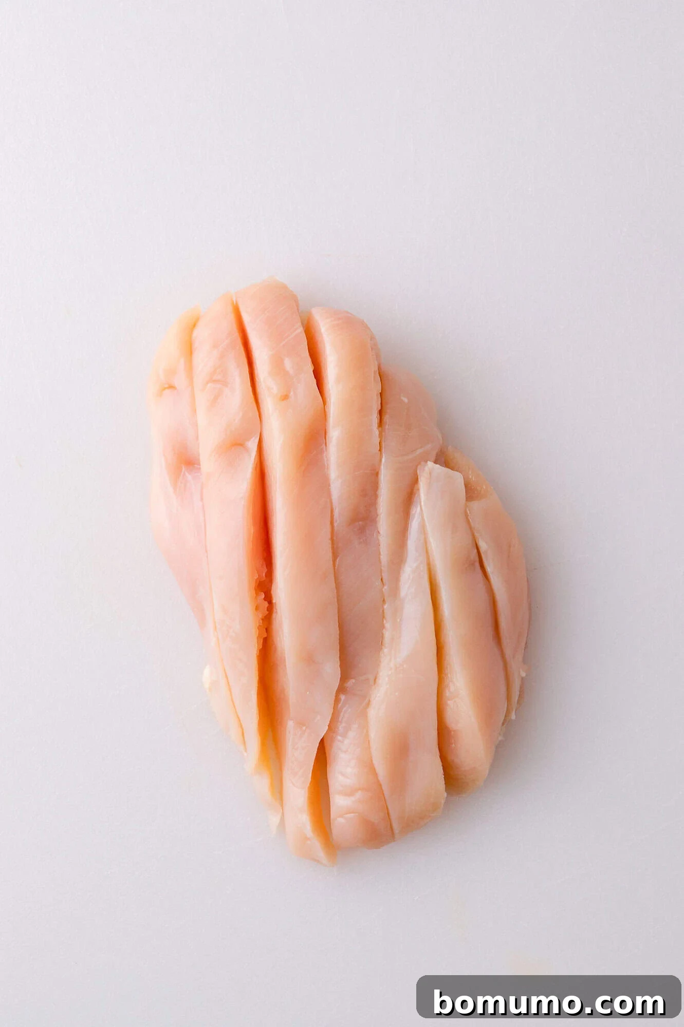 Raw chicken breast sliced into strips on a white cutting board.
