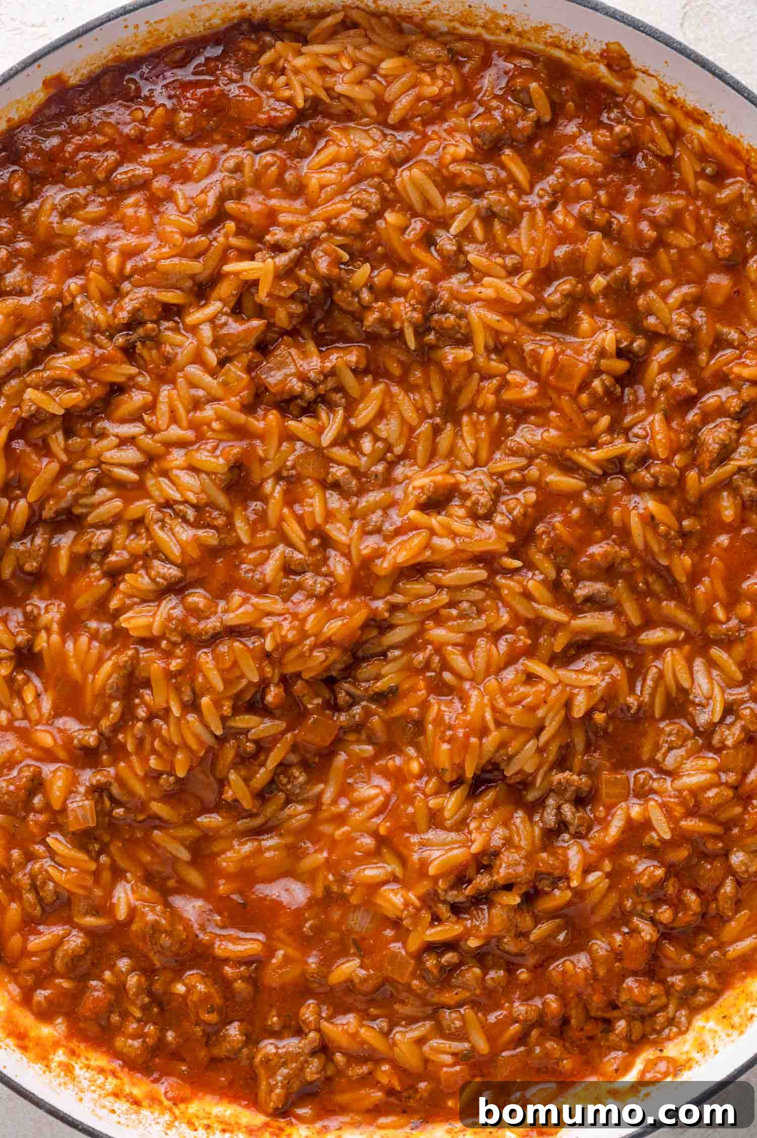 A close-up of a pan filled with cooked ground beef, orzo, and tomato sauce mixed together.