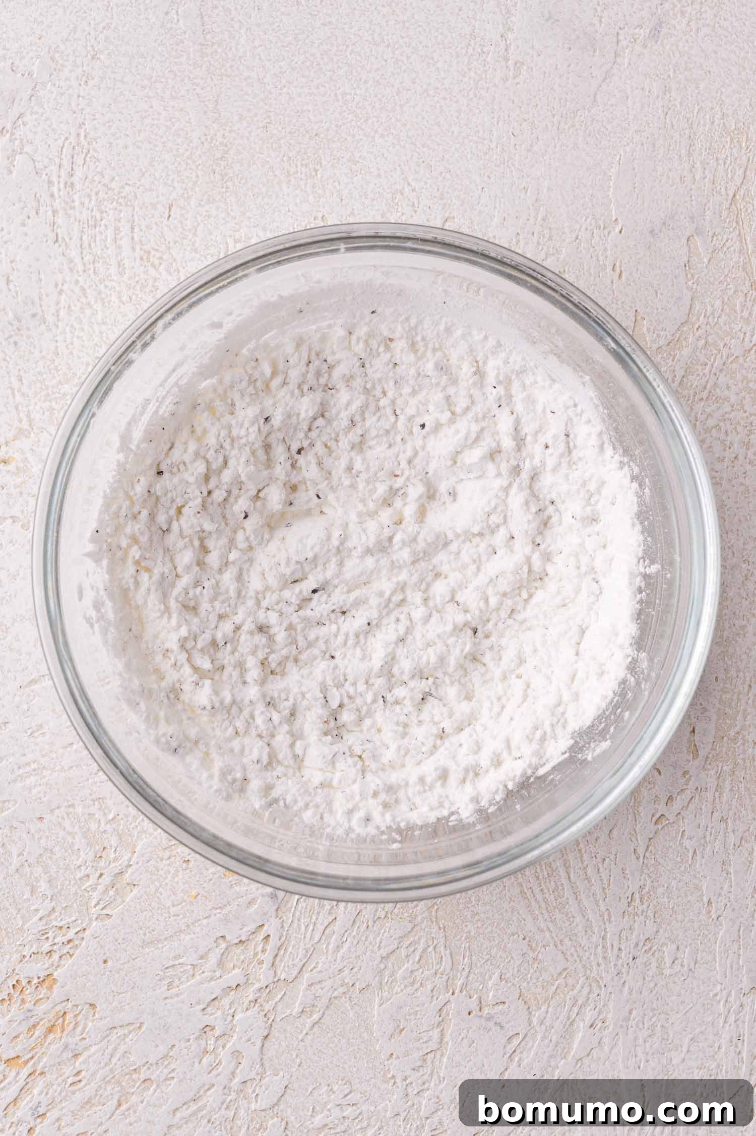 A clear glass bowl filled with a cornstarch mixture sits on a textured light-colored surface.