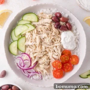 A vibrant Greek chicken bowl with shredded chicken, fresh cucumbers, cherry tomatoes, Kalamata olives, red onions, and a dollop of creamy tzatziki sauce, served over fluffy rice.