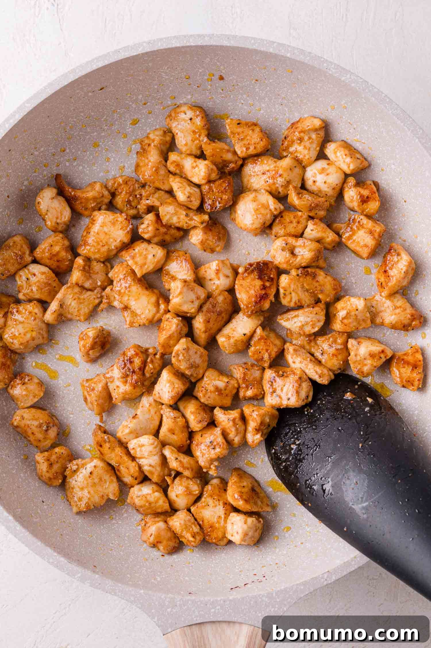 Perfectly cooked, seasoned chicken breast pieces sizzling in a frying pan, with a black spatula poised to stir, showcasing the golden-brown crust.