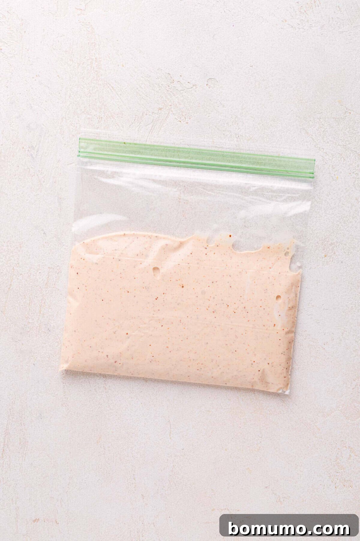 The finished creamy sauce is securely stored in a sealed plastic zip-lock bag, ready for easy drizzling, placed on a subtly textured surface.