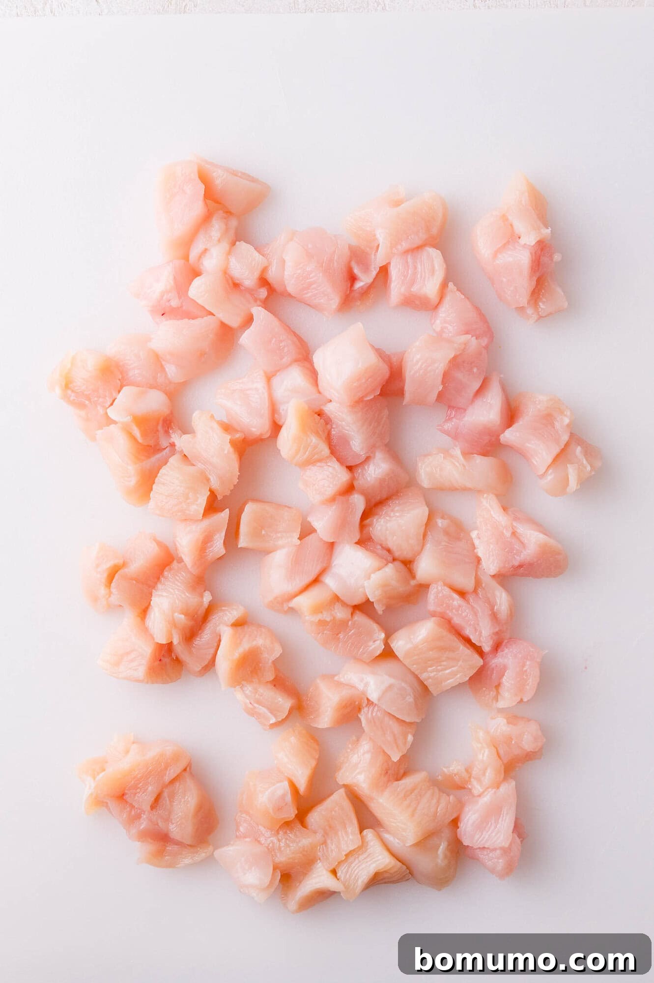 Raw chicken breast expertly cut into small, evenly sized cubes, arranged neatly on a clean white cutting board, ready for seasoning and cooking.