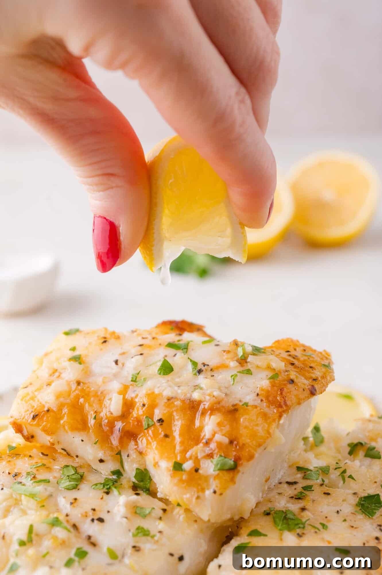 Golden Lemon Butter Cod 11 A hand squeezes a fresh lemon wedge over a plated serving of lemon butter cod, ready to be enjoyed.