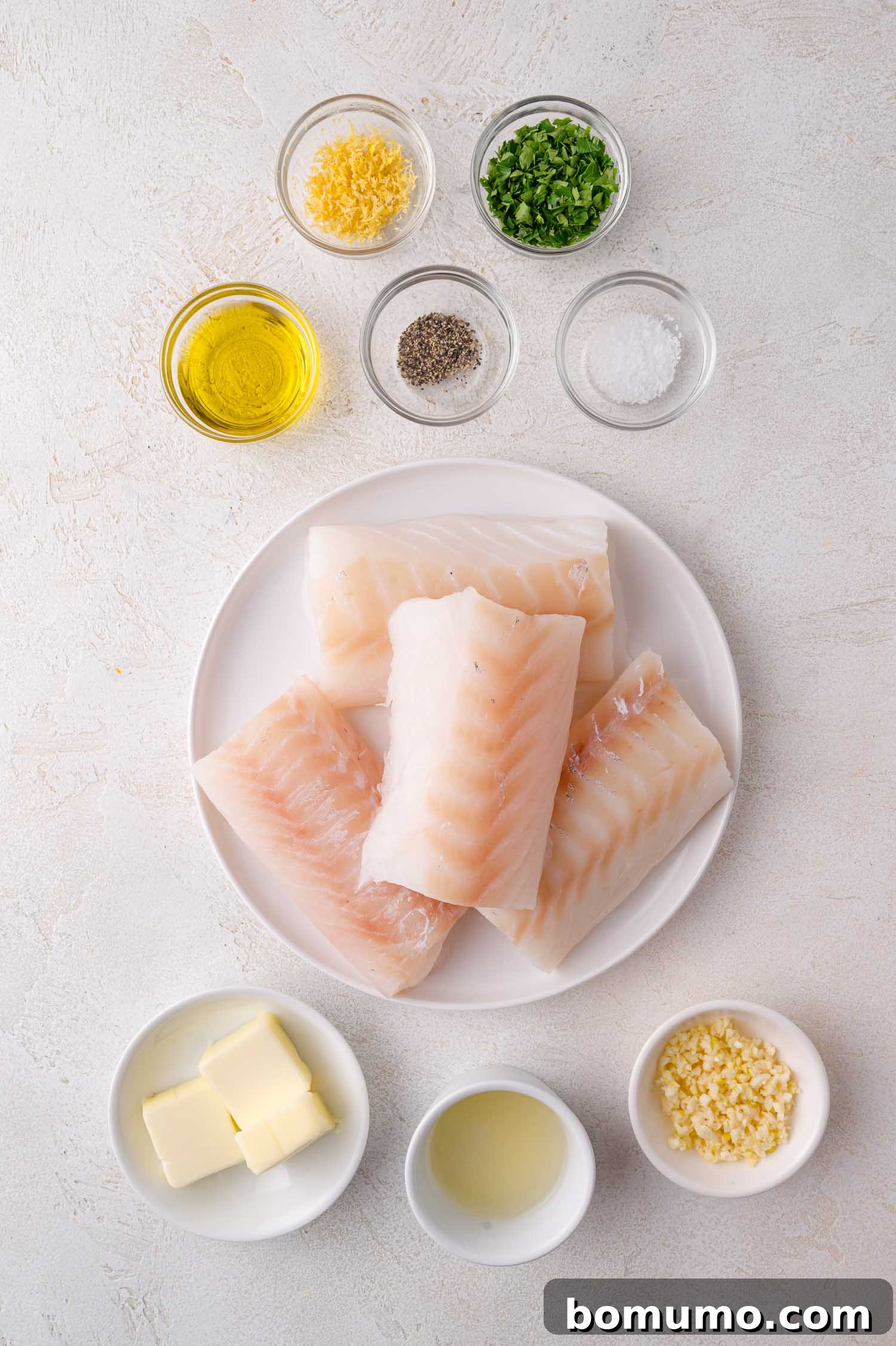 Golden Lemon Butter Cod 3 All ingredients for lemon butter cod arranged on a white surface, including raw cod, butter, lemon, and spices.