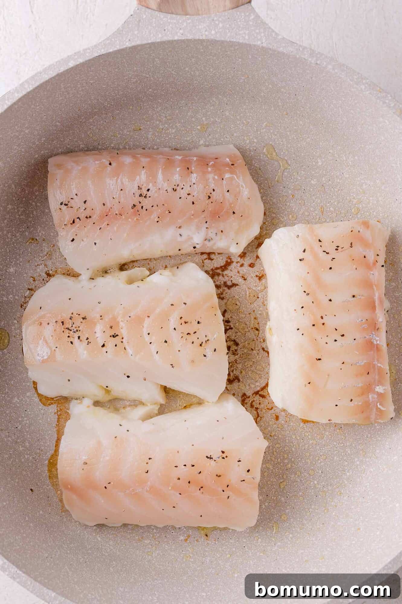Golden Lemon Butter Cod 5 Seasoned cod fillets searing in a hot pan to create a golden crust.