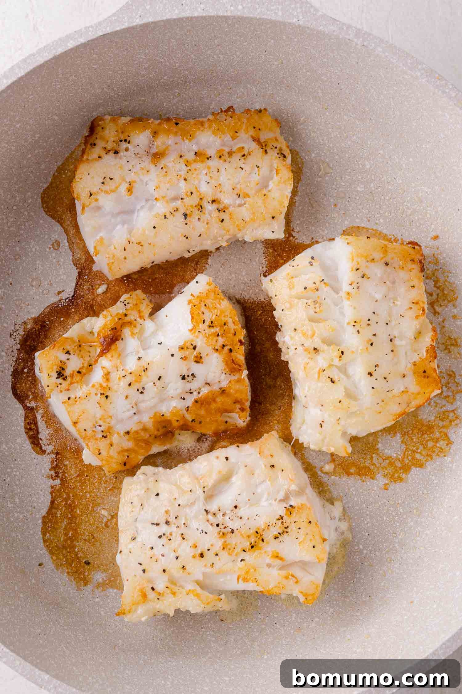 Golden Lemon Butter Cod 6 Cod fillets being flipped in the pan, showing a perfectly golden-brown seared side.