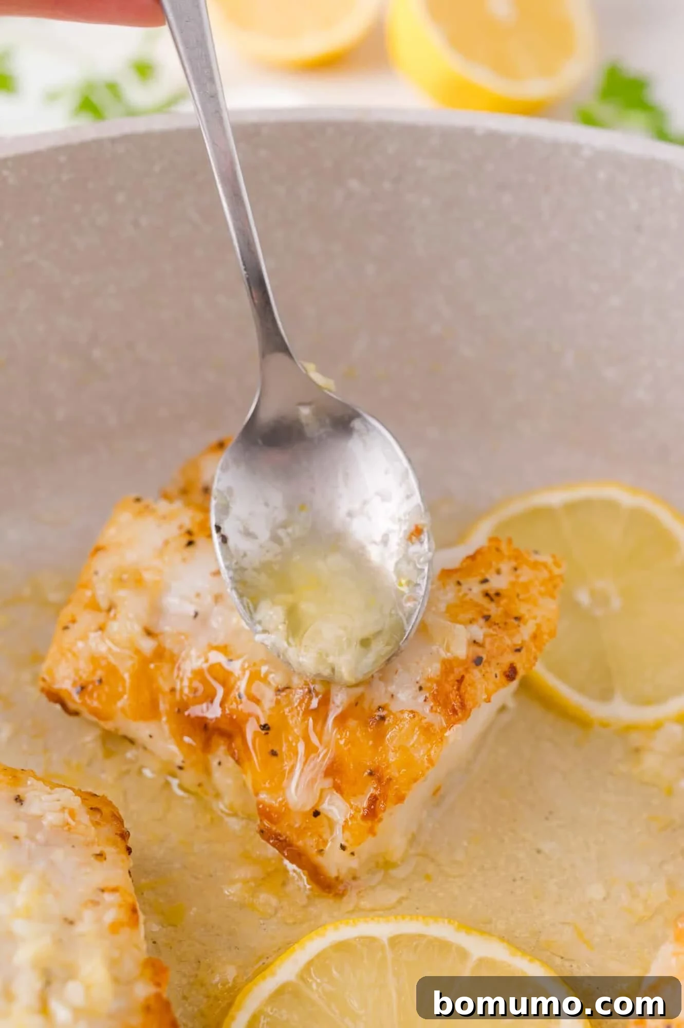 Golden Lemon Butter Cod 10 A spoon basting the seared cod fillets with the finished lemon butter sauce in the skillet.