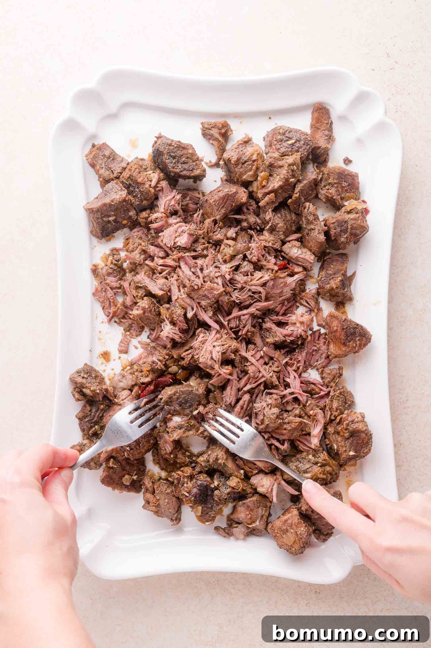 Effortless Shredded Barbacoa 11 Two forks being used to shred the tender, cooked beef on a white plate.