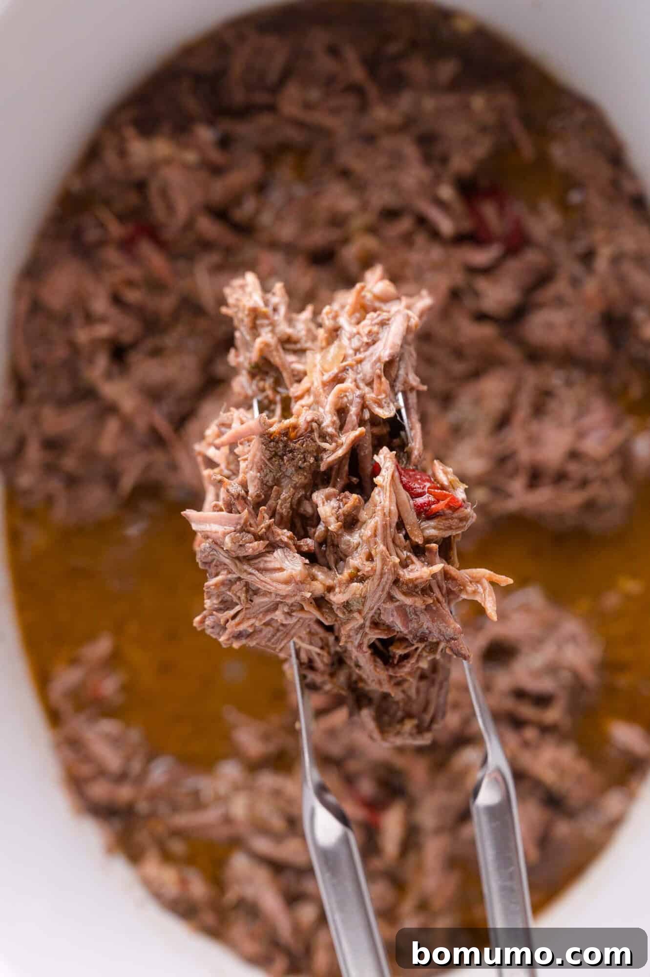 Effortless Shredded Barbacoa 12 A close-up of the juicy shredded beef barbacoa being lifted with tongs from the slow cooker.