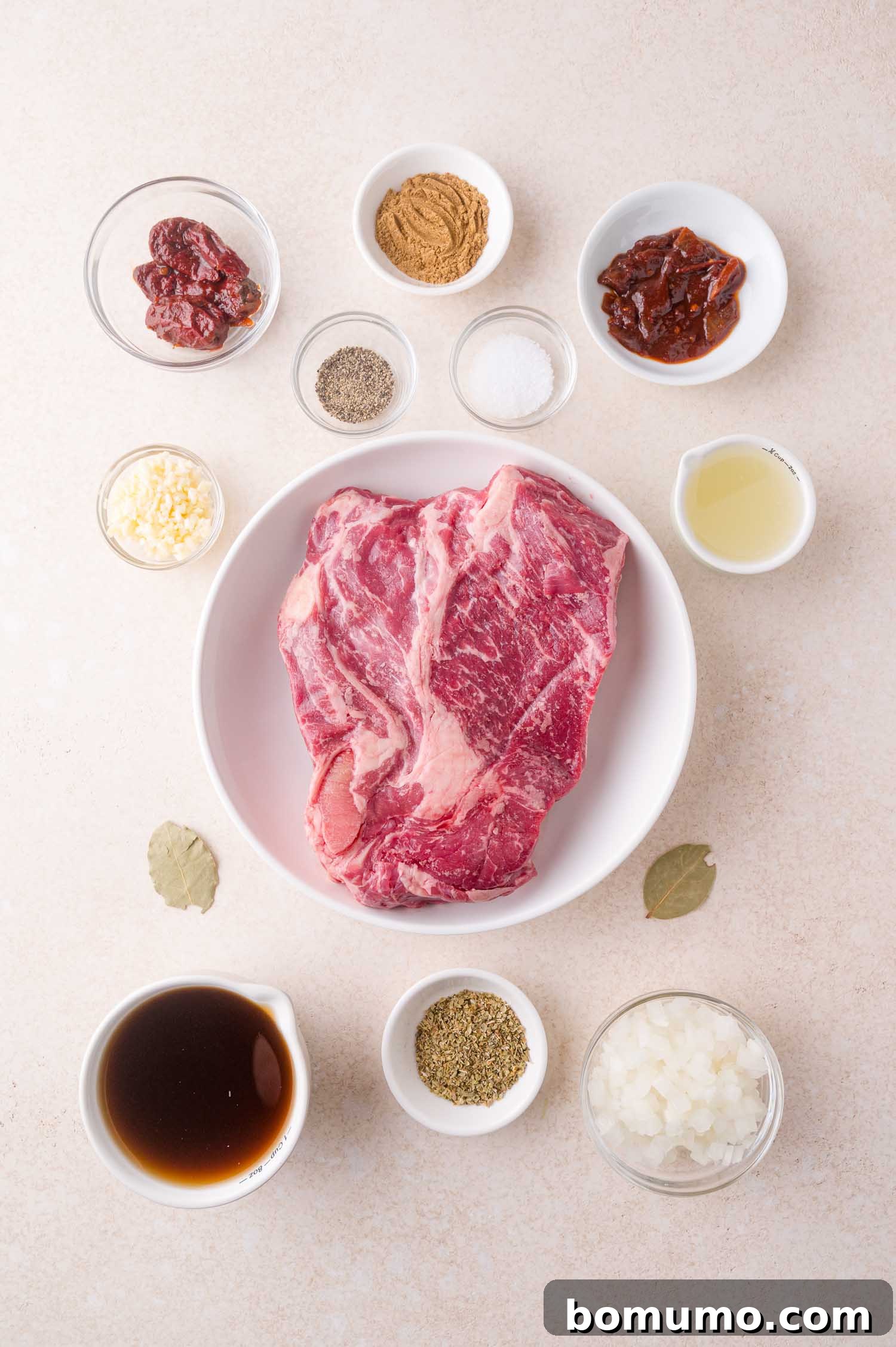 Effortless Shredded Barbacoa 4 All ingredients for the barbacoa recipe, including a raw beef roast and various spices in bowls, arranged on a countertop.
