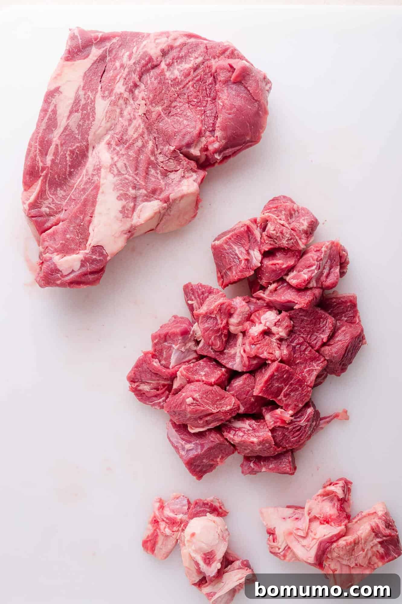 Effortless Shredded Barbacoa 5 A raw beef chuck roast being cut into large chunks on a white cutting board.