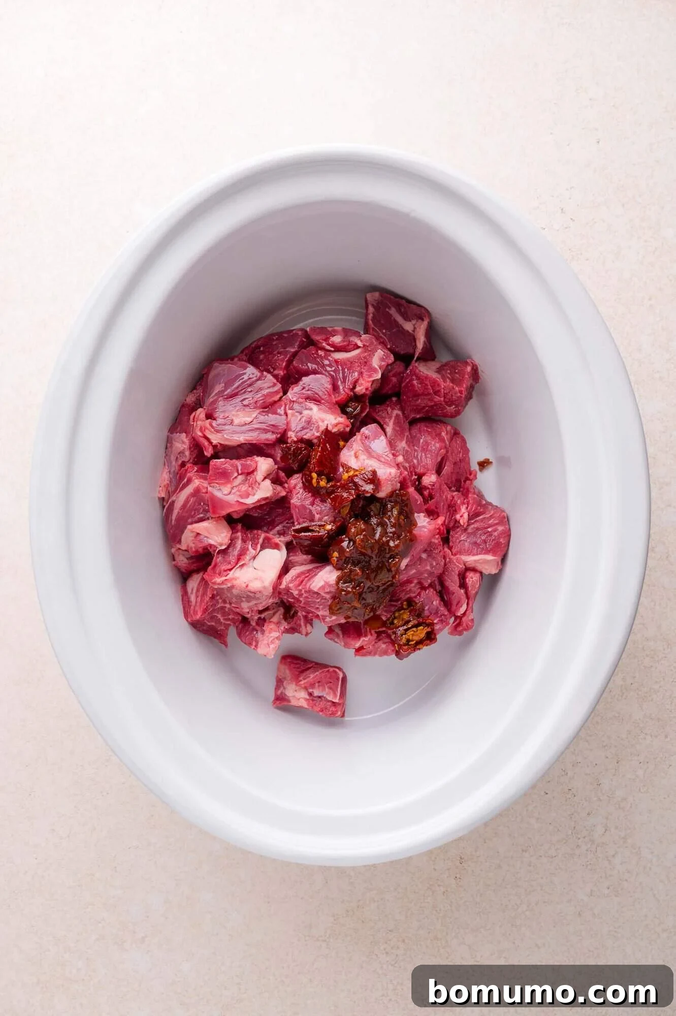 Effortless Shredded Barbacoa 7 The raw beef chunks and chipotle peppers are placed inside a white slow cooker liner.